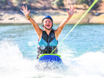 A camper with their hands in the air while kneeboarding.