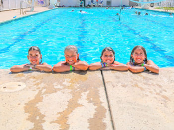 Campers leaning on the edge of the pool and smiling.