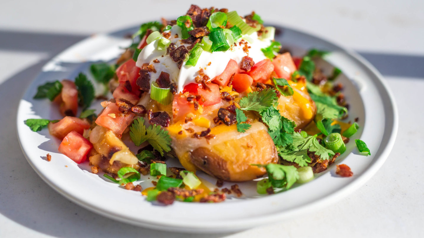A baked potato with taco topping including tomatoes, lettuce, and sour cream.