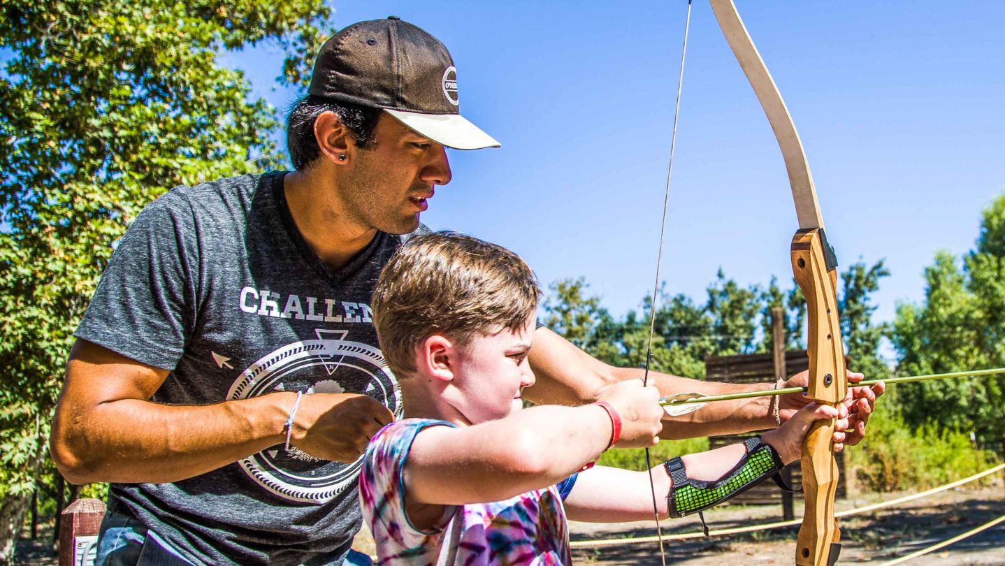 A camper learning how to shoot a bow and arrow
