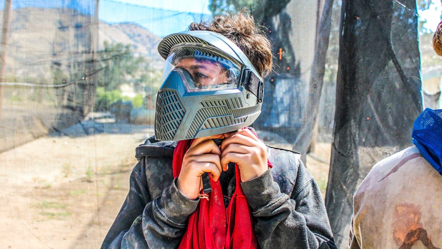 A camper adjusting their helmet before playing paintball