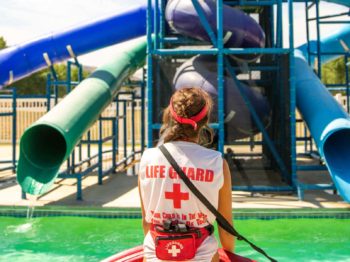 A lifeguard standing by the pool and water slide.